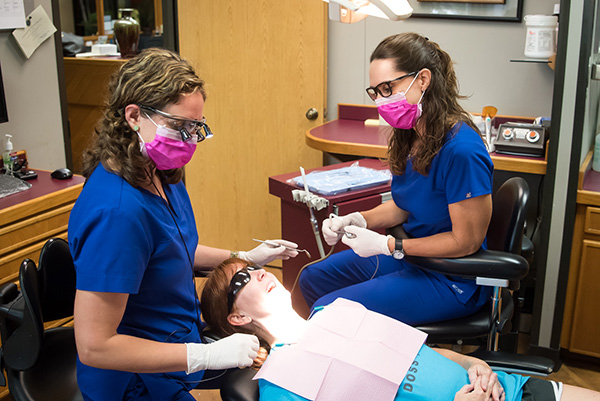 Two dental professionals treating a patient wearing protective pink masks.