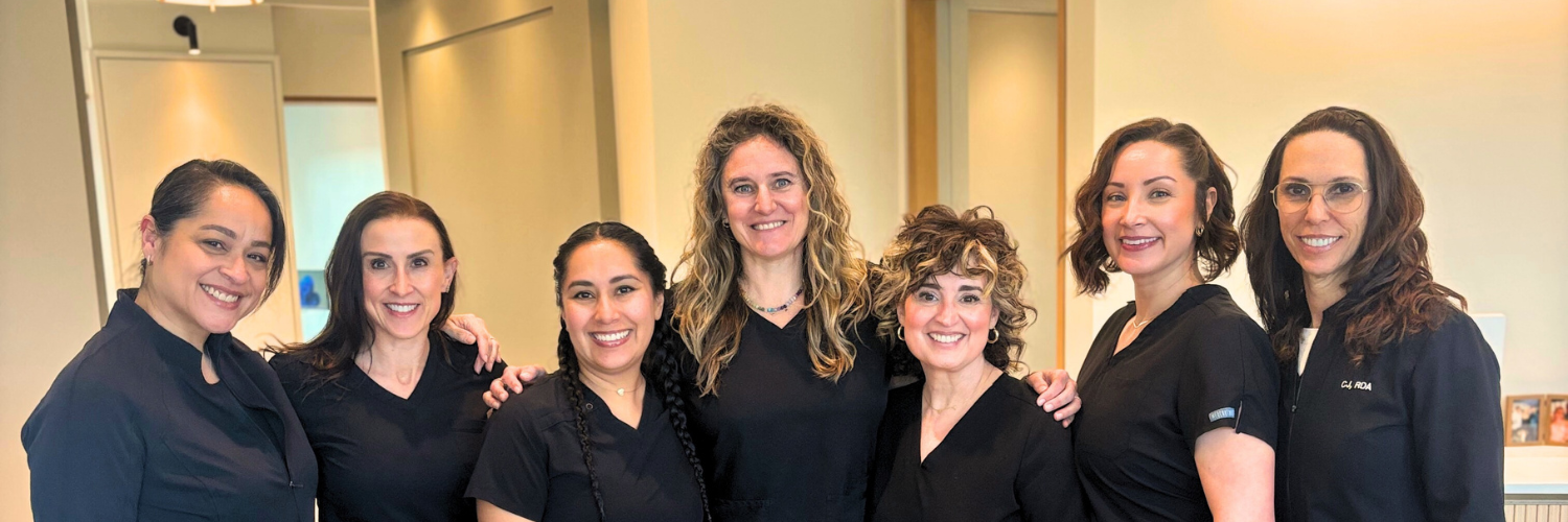 Three women smiling together in a well-lit indoor setting.